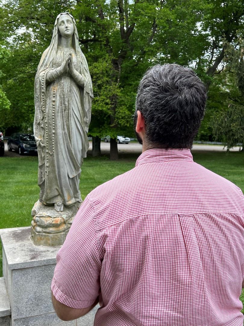 Man praying at a statue of mary